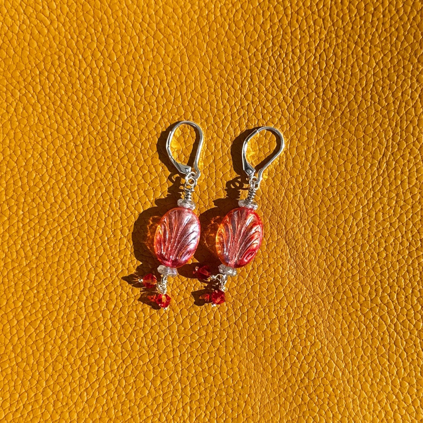 Pair of earrings with red and clear glass beads on a yellow textured background