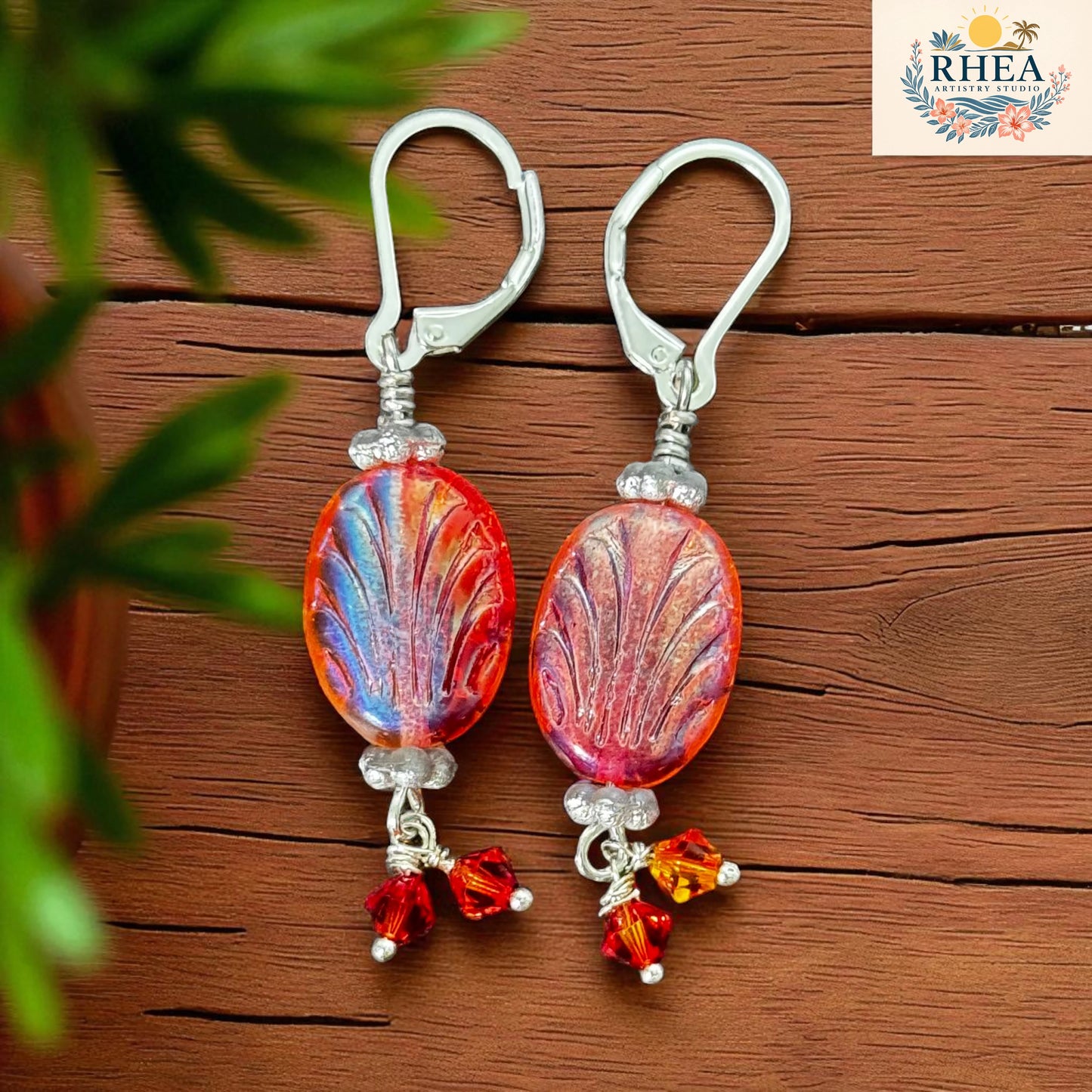 Pair of earrings with colorful glass beads on a wooden surface, branded 'RHEA'.
