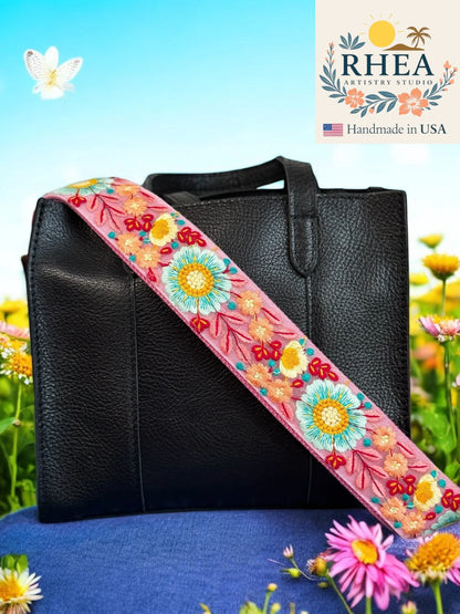 Black leather bag with a colorful floral purse strap against a natural background, featuring the RHEA brand.