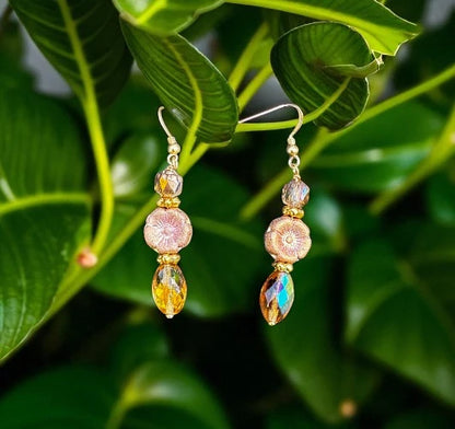 Pair of gold and multicolored bead earrings on a green leaf background