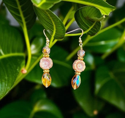 Pair of gold and multicolored bead earrings on a green leaf background