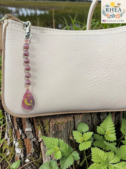 Handmade Pink and mauve beaded bag charm with brass accents and hand-painted pendant on a cream bag