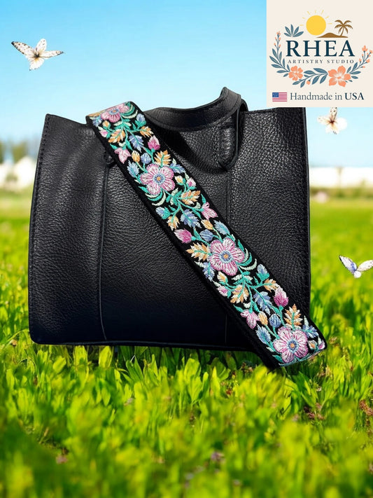 Black handbag with floral purse strap on grass, RHEA brand visible