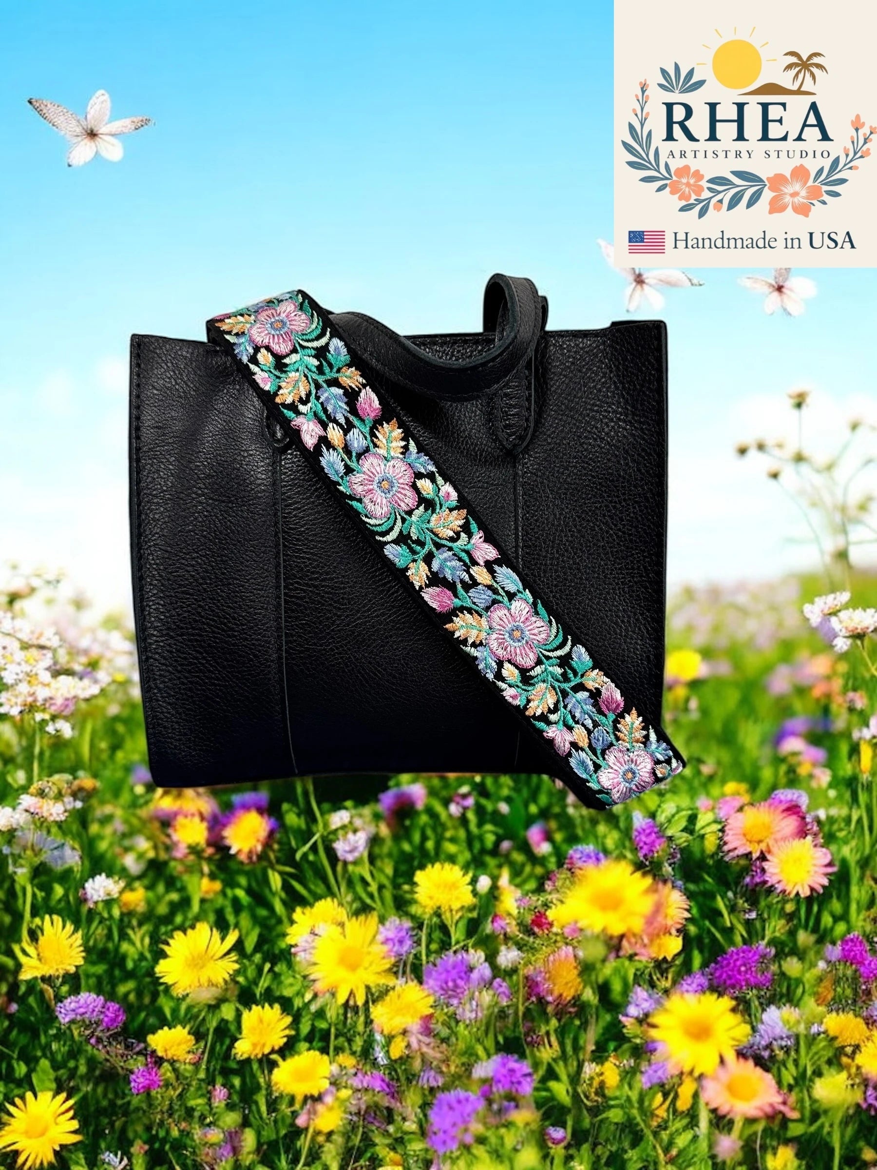Black handbag with a floral purse strap in a field of flowers, featuring the RHEA Artistry Studio logo.