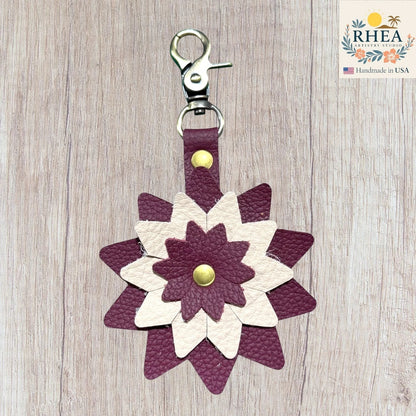 Floral-patterned keychain with purple and white design on a wooden surface, Handcrafted leather floral charm designed for purses and totes