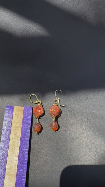 A pair of handcrafted Czech glass earrings with a serene glow, featuring a combination of rusty pink and brick orange hues, with brass hardware.