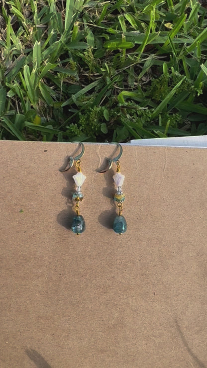 A pair of gold-colored three petal cathedral drop earrings with white and blue czech glass accents, displayed against a beige background.