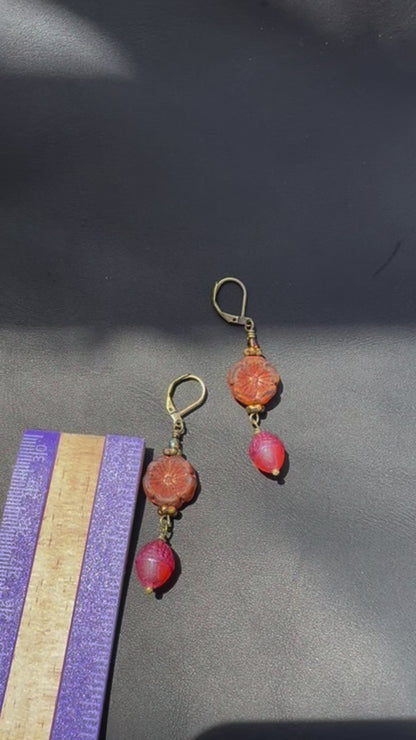 A pair of handcrafted Czech glass earrings with a serene glow, featuring a combination of rusty pink and brick orange hues, with brass hardware.
