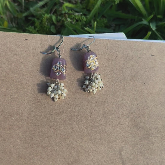 Silver earrings with a mauve color cluster of pearls and a hand painted glass bead, displayed on a spiral notebook page with grass and shadows in the background.