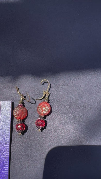 A pair of handcrafted Czech glass earrings with a serene glow, featuring a combination of rusty pink and brick orange hues, with brass hardware.