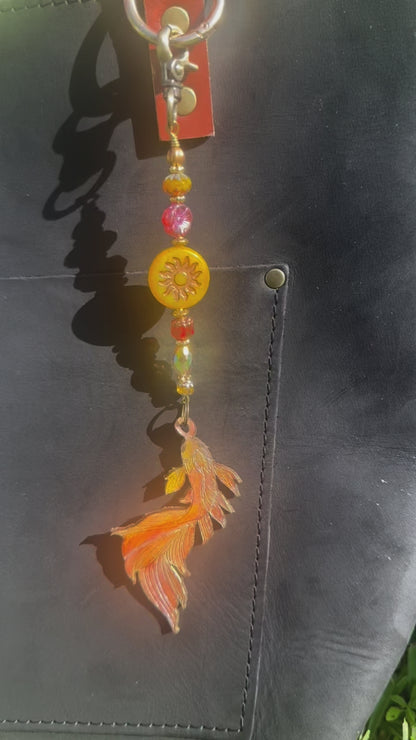 A handcrafted leather charm with a koi fish design, featuring solid brass hardware and high-end designer quality Czech glass, attached to a black leather strand.