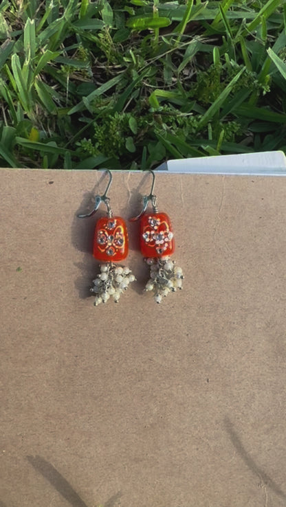 Red earrings with floral designs and pearl-like beads on a old book