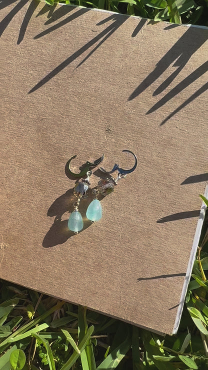 A pair of cathedral-shaped silver drop earrings with light blue colored glass.