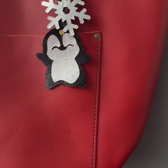 Handcrafted leather charm featuring a laughing penguin with a silver snowflake on top. The charm is designed in a sleek black and silver color combination and includes a lobster clasp for easy attachment to purses or use as a keychain.