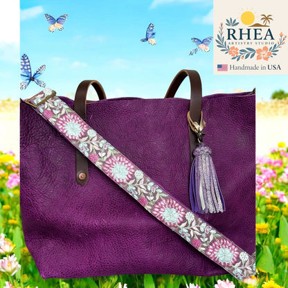 Purple handbag with a floral purse strap and tassel against a colorful background with flowers and butterflies, featuring the RHEA Artistry Studio logo.