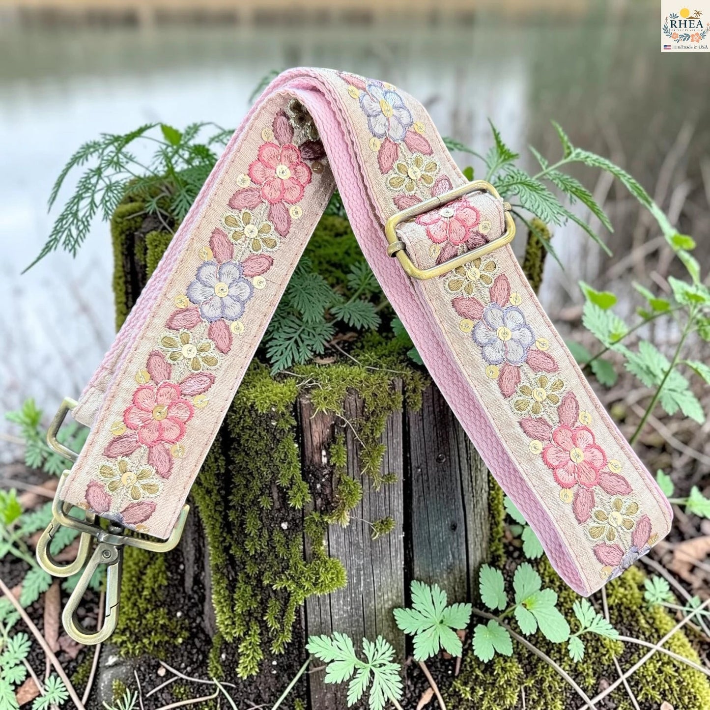A floral canvas shoulder strap with pink, blue, and yellow embroidered flowers, resting on a mossy wooden stump outdoors.