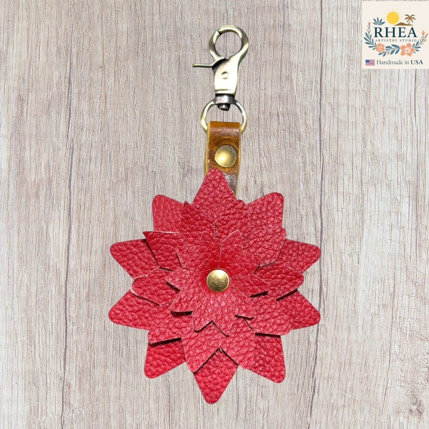 Red flower-shaped keychain with a gold clasp on a wooden surface, f. Floral leather keychain handcrafted with brass-tone hardware