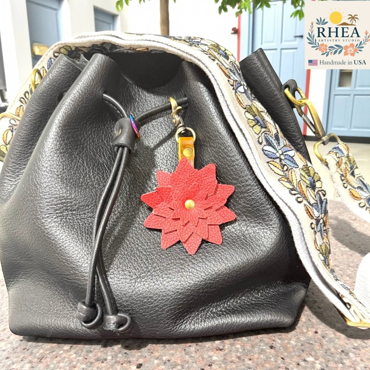Black leather bag with a red flower charm on a textured surface. Leather flower keychain with swivel lobster clasp detail