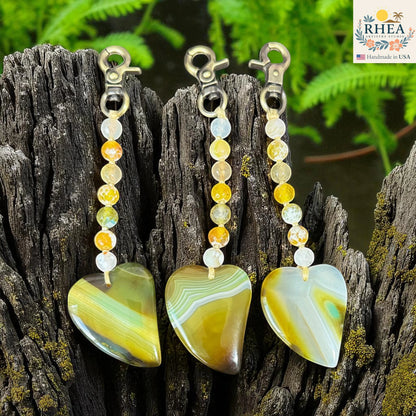 Rhea Artistry Studio handmade agate heart bag charms with brushed brass clasps and yellow, white, and green gemstone beads.