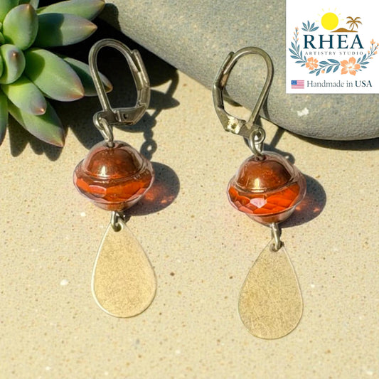 Rhea Artistry Studio handcrafted drop earrings with faceted amber glass beads and brushed brass teardrops, 2 inches long.