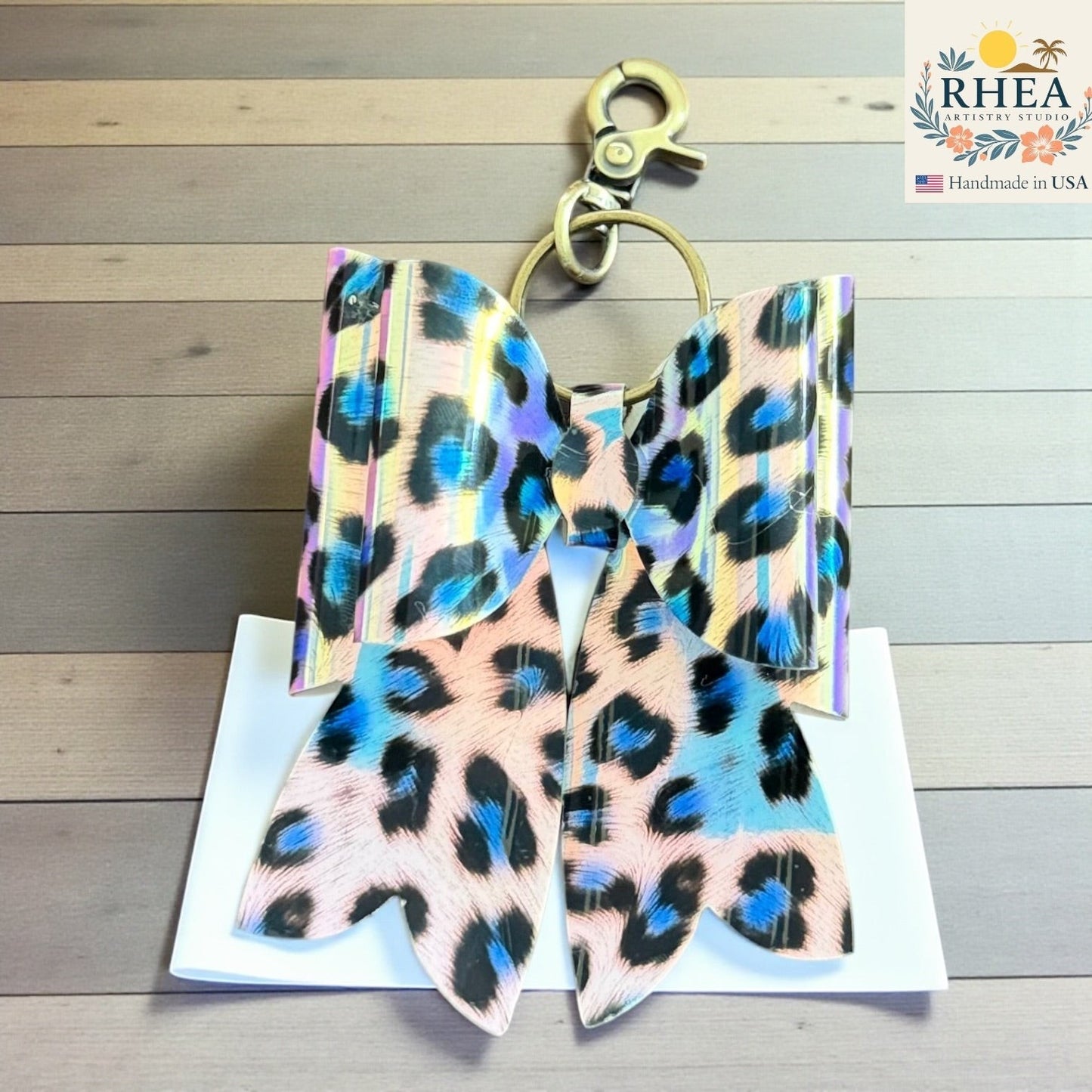 Rhea Artistry Studio handmade animal print bow bag charm with brass hardware. Features holographic finish and double-layer French bow design.