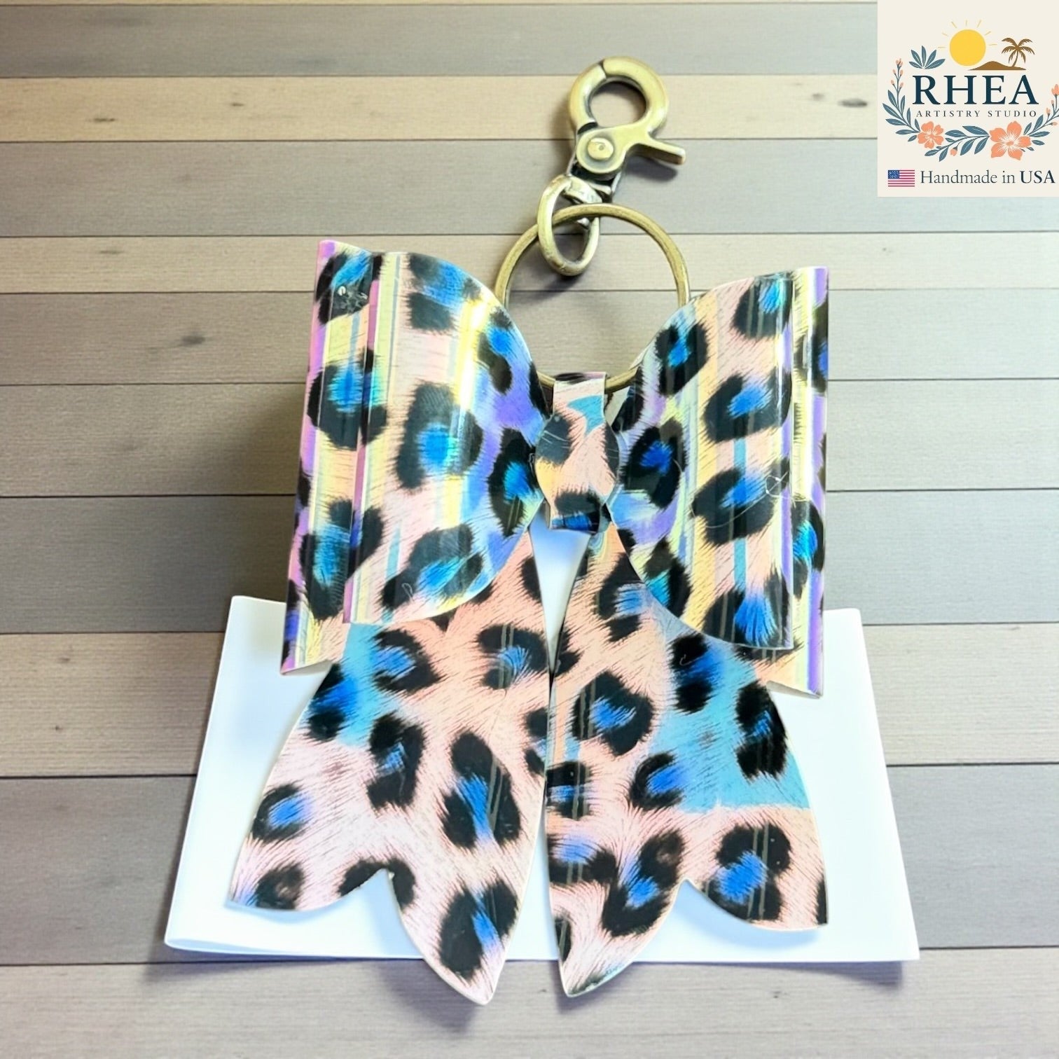Rhea Artistry Studio handmade animal print bow bag charm with brass hardware. Features holographic finish and double-layer French bow design.