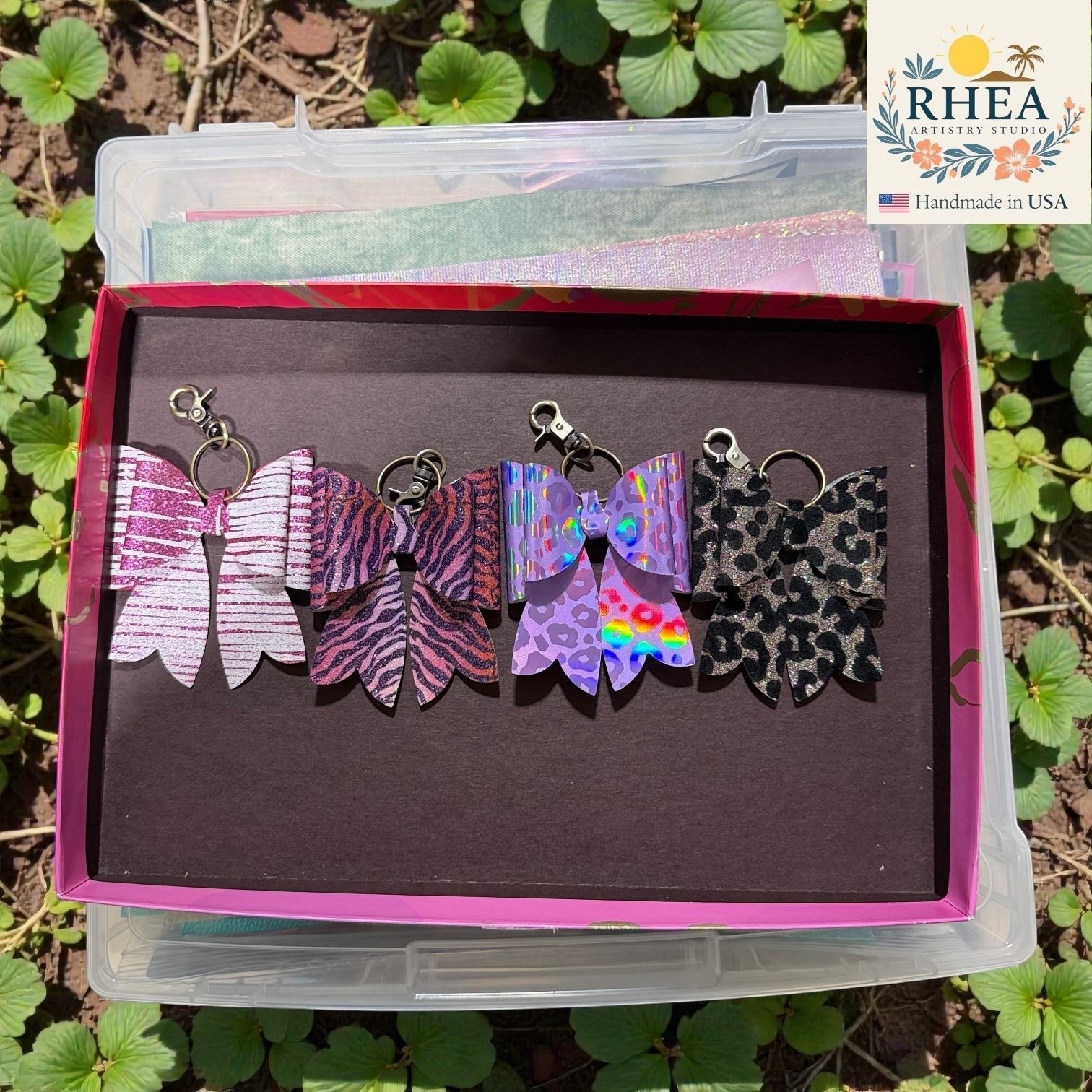 Rhea Artistry Studio handmade animal print bow bag charms in pink glitter, zebra, purple holographic, and leopard patterns with brass hardware.
