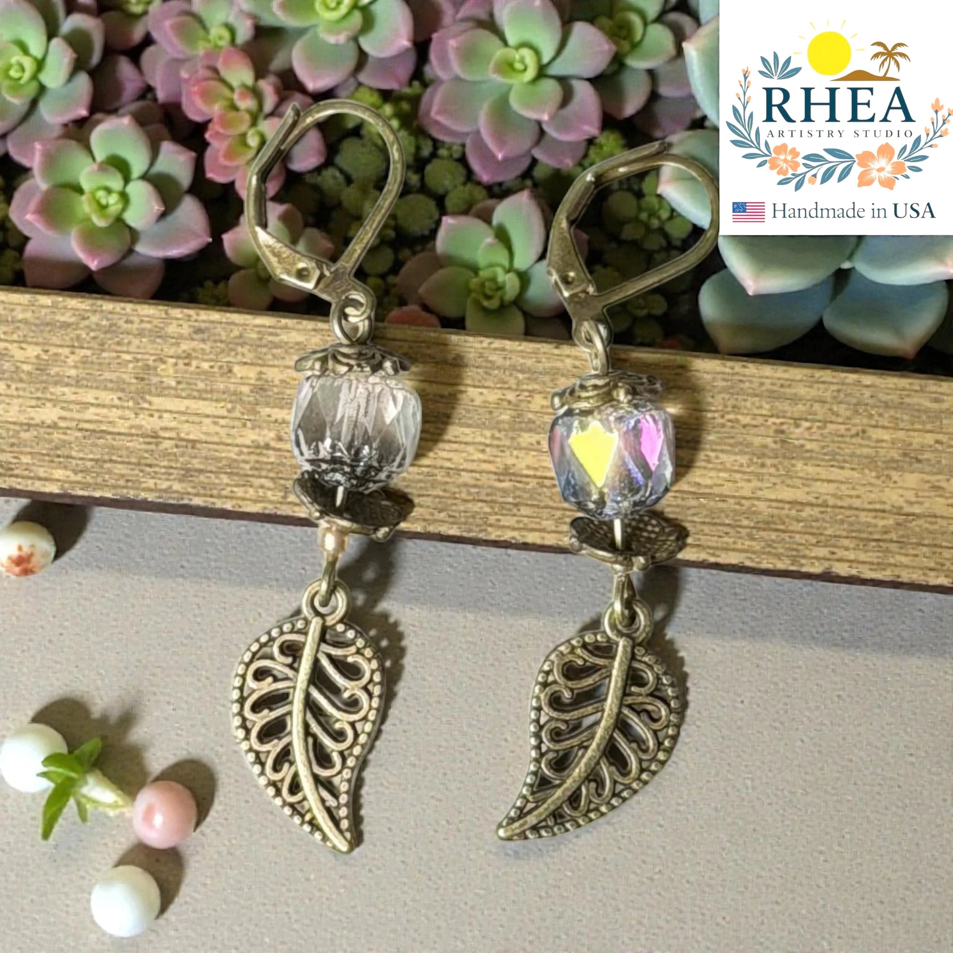 Rhea Artistry Studio antique brass leaf drop earrings with clear faceted glass beads and Bali-style spacers, 2 inches long.