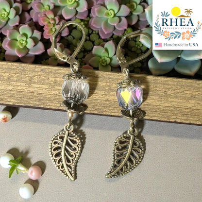 Rhea Artistry Studio antique brass leaf drop earrings with clear faceted glass beads and Bali-style spacers, 2 inches long.