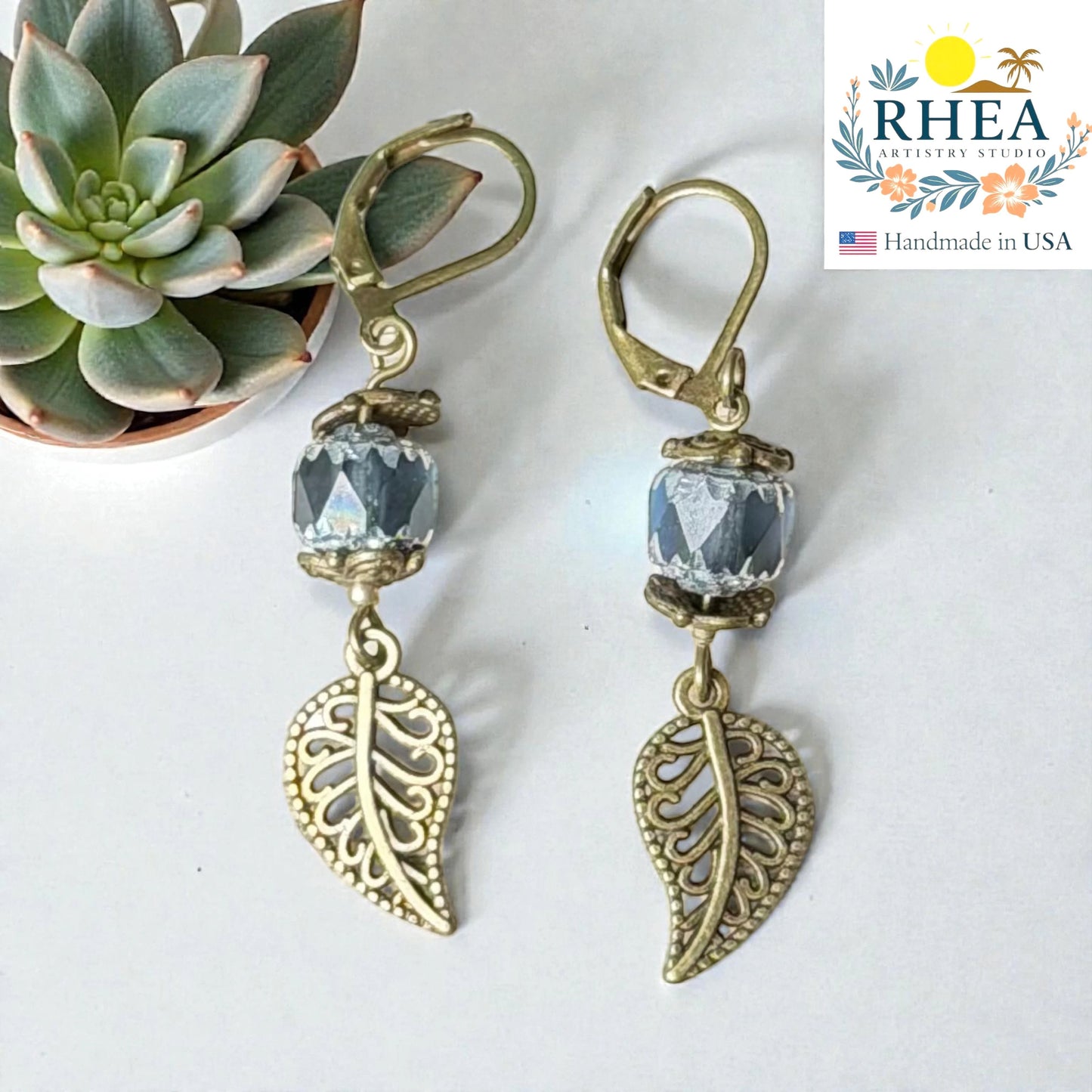 Rhea Artistry Studio antique brass leaf drop earrings with faceted blue glass beads, approx. 2 inches long.