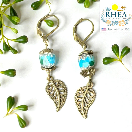 Rhea Artistry Studio antique brass leaf drop earrings with blue faceted glass beads and Bali-style spacers, approx. 2 inches long.