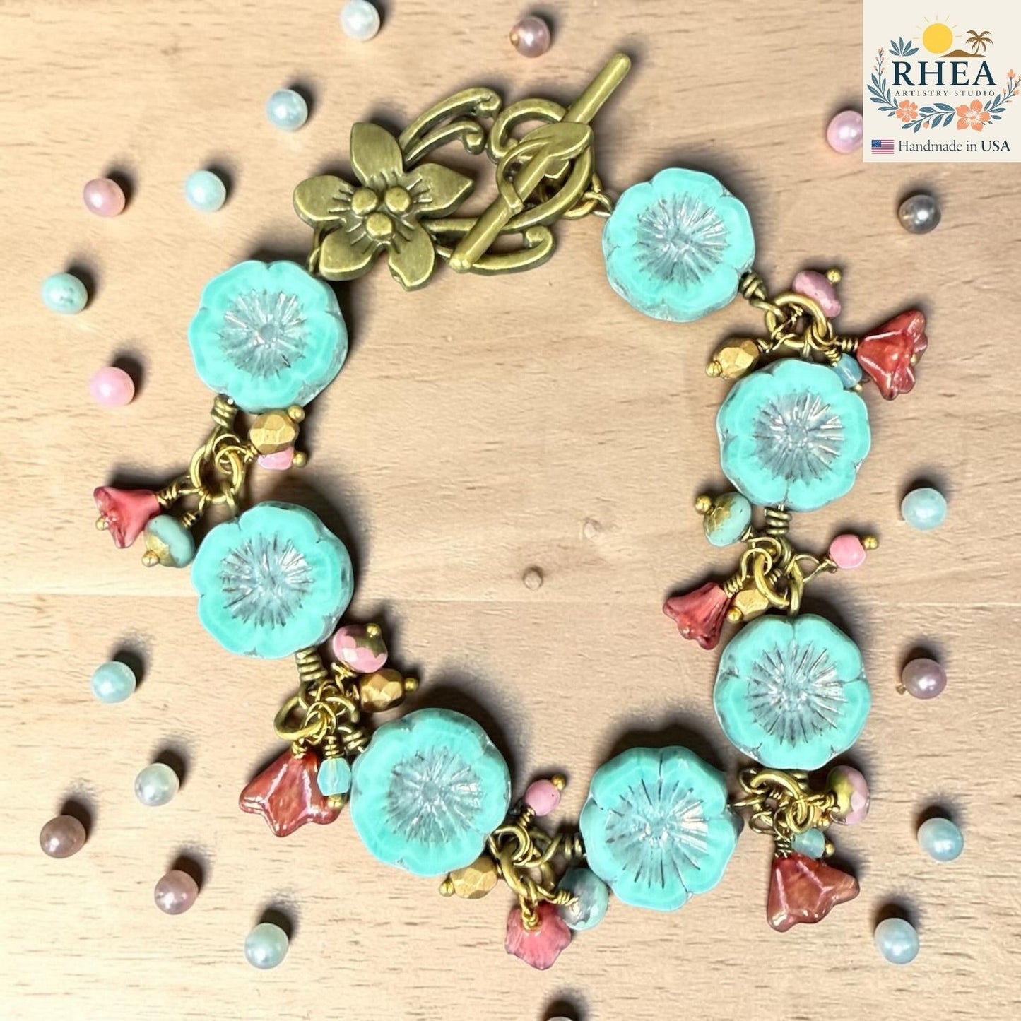 Rhea Artistry Studio handmade bracelet with aqua blue glass flower beads, pink floral charms, and antique brass toggle clasp.