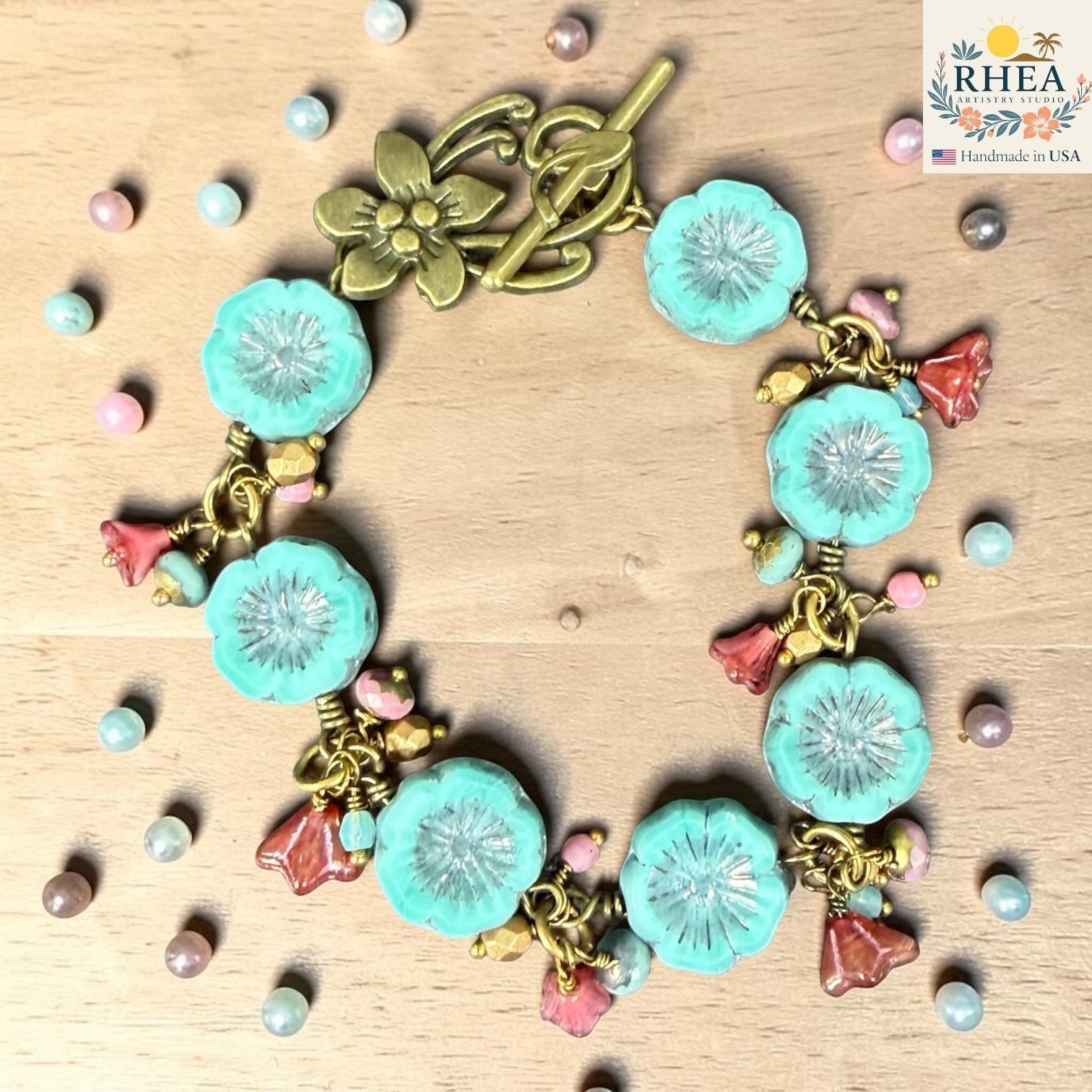 Rhea Artistry Studio handmade bracelet with aqua blue glass flower beads, pink floral charms, and antique brass toggle clasp.