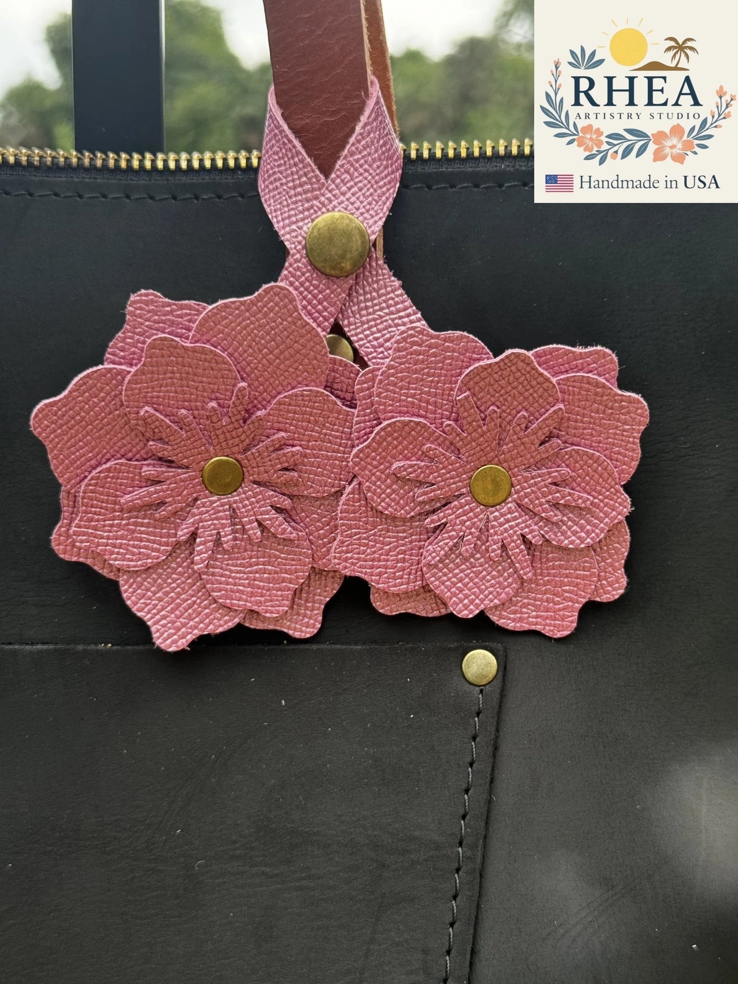 Rhea Artistry Studio Barbie Pink double leather flower charm with brass rivets, attached to a black leather bag.