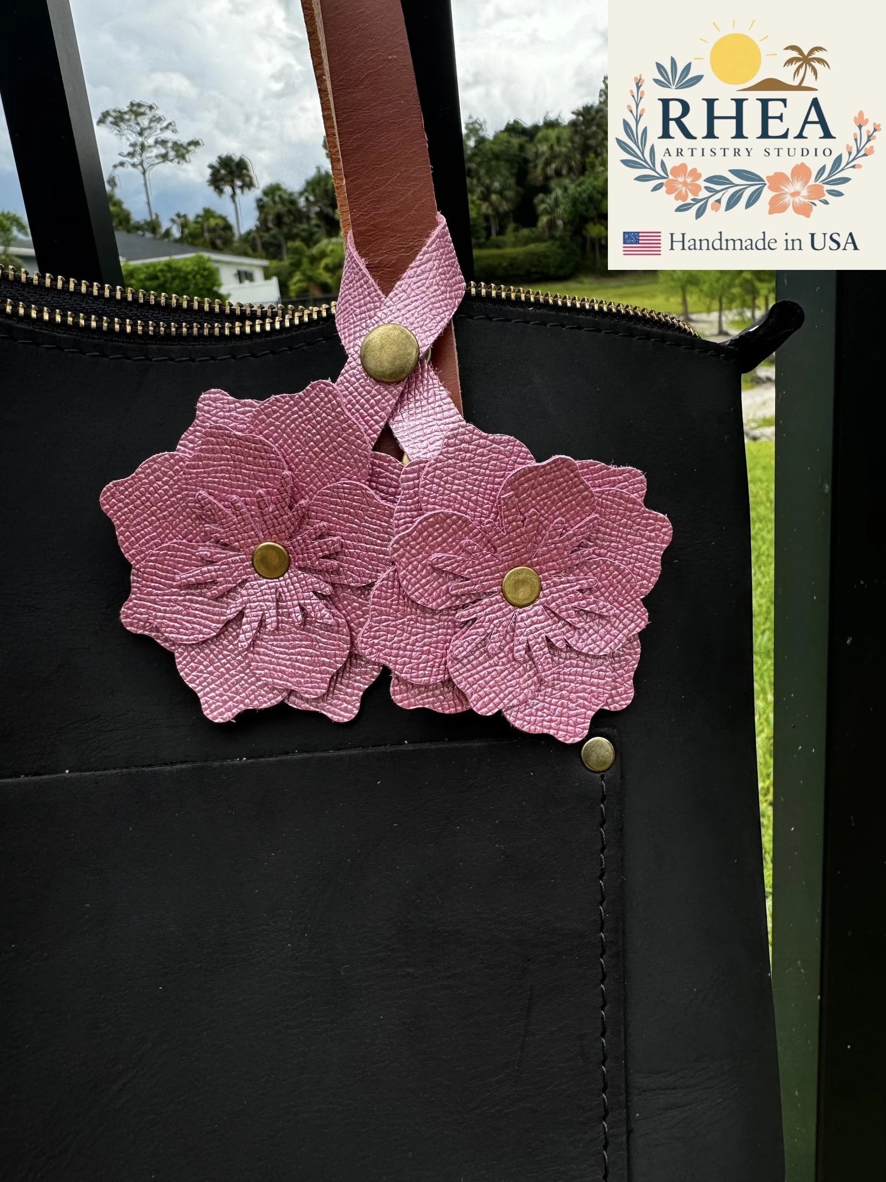 Rhea Artistry Studio Barbie Pink double leather flower charm with brass rivets attached to a black leather bag.