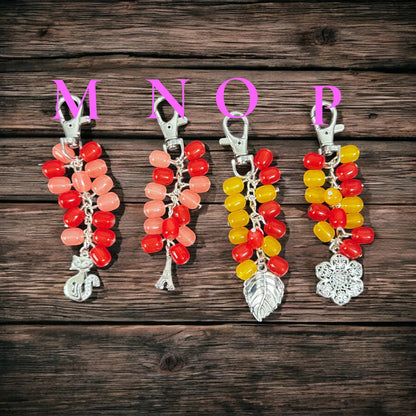 Rhea Artistry Studio handmade beaded keychains in red, pink, and yellow with silver charms: cat, Eiffel Tower, leaf, and snowflake.