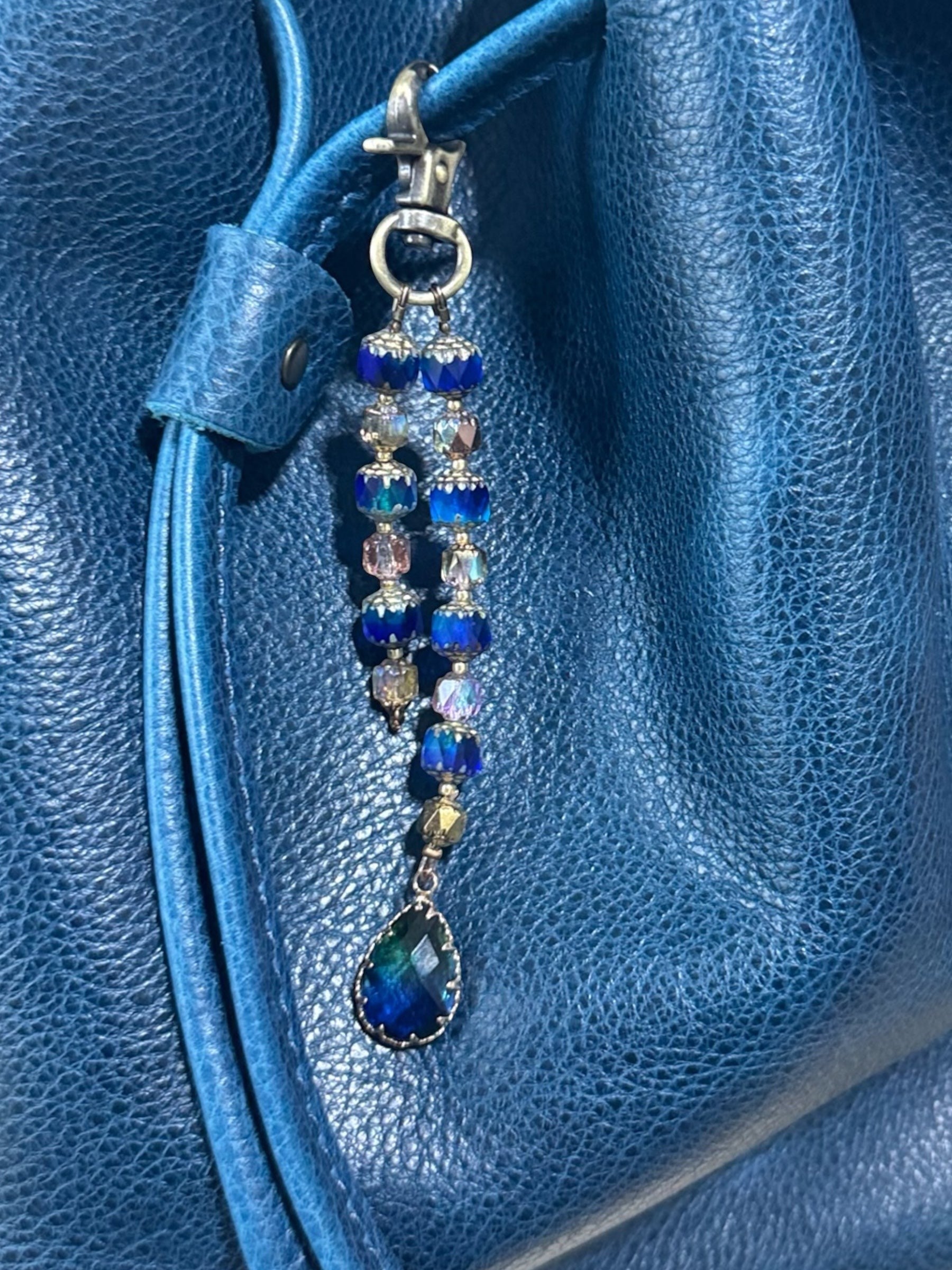 Rhea Artistry Studio elegant beaded keychain with blue crystal beads, brass accents, and a teardrop pendant, attached to a blue leather bag.