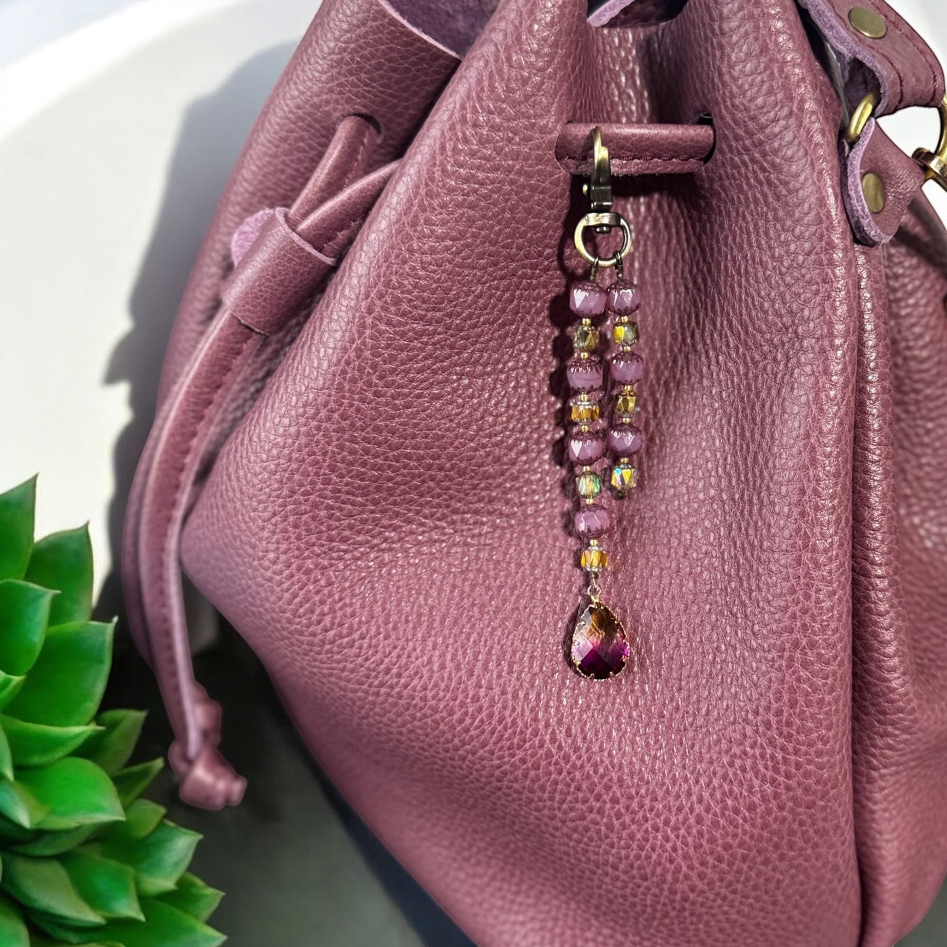 Rhea Artistry Studio elegant beaded keychain with purple teardrop pendant and brass accents, attached to a plum leather bag.