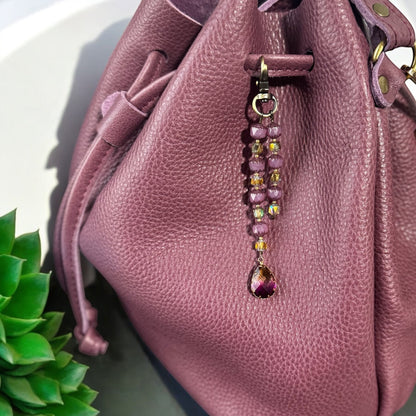 Rhea Artistry Studio elegant beaded keychain with purple teardrop pendant and brass accents, attached to a plum leather bag.