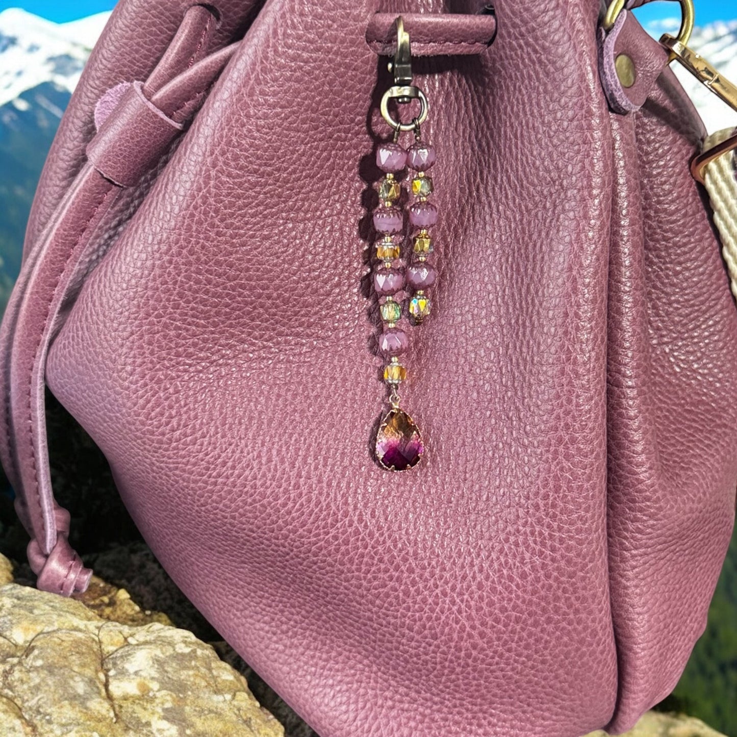 Rhea Artistry Studio elegant beaded keychain with teardrop pendant, featuring purple and gold beads and brass accents, attached to a plum leather bag.