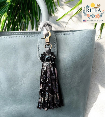 Rhea Artistry Studio handmade black leather tassel bag charm with holographic geometric pattern and lobster clasp.