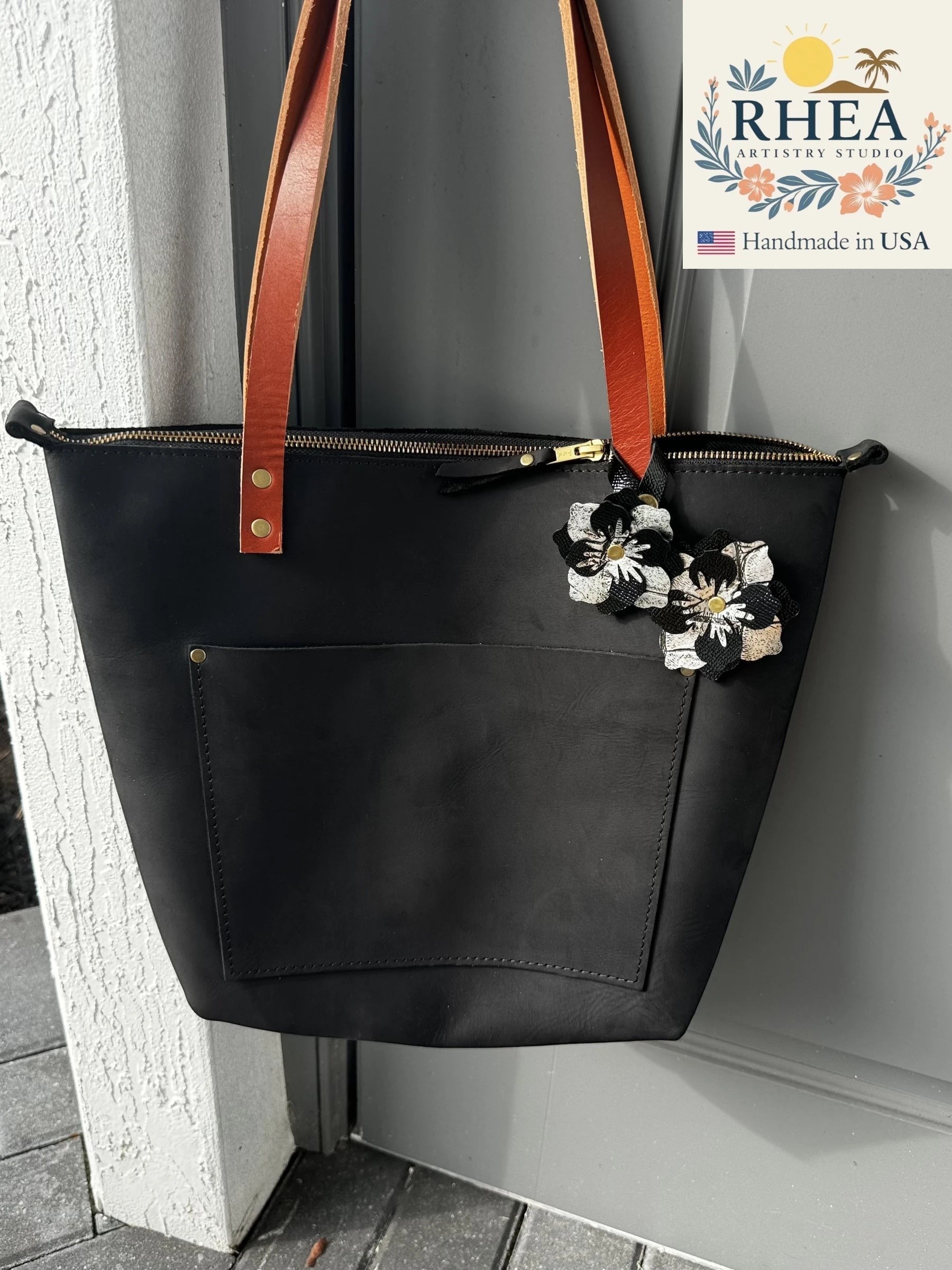 Rhea Artistry Studio black leather tote bag with two leather flower charms, one sparkly black and one silver alligator embossed.