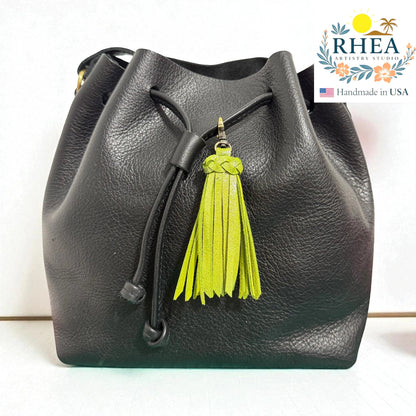 Rhea Artistry Studio black leather drawstring bucket bag with a bright lime green leather tassel charm and antique brass clasp.