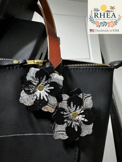 Rhea Artistry Studio black and silver leather flower double charm with brass rivets and snap fastener attached to a black leather bag.