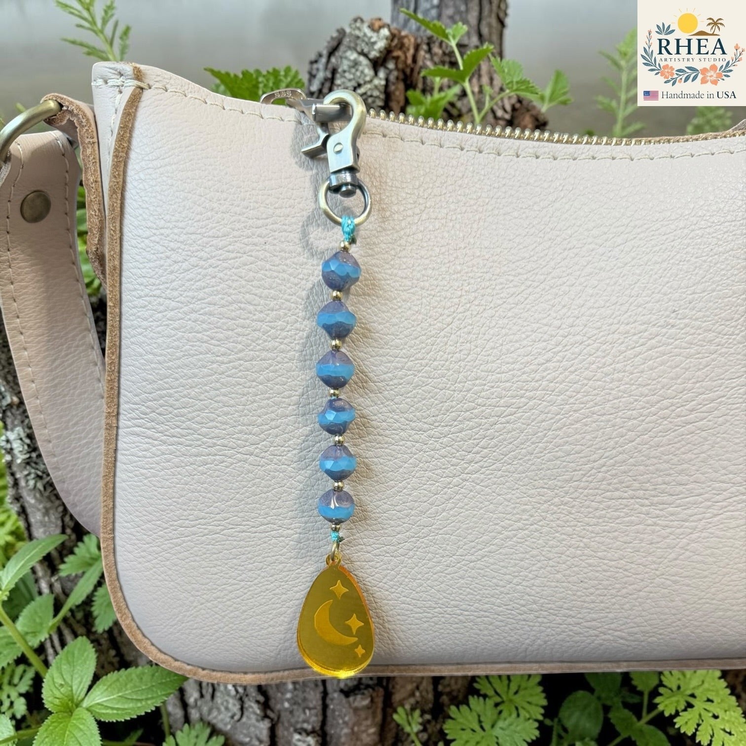 Rhea Artistry Studio blue Czech glass bead bag charm with brass accents and a yellow teardrop pendant featuring crescent moons and stars.