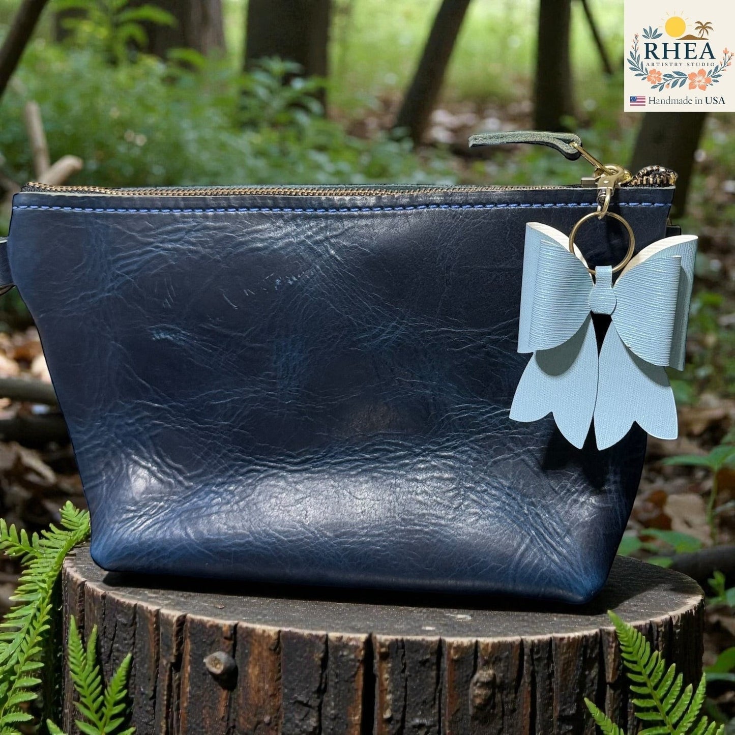 Rhea Artistry Studio light blue double-layer French bow bag charm with brass hardware attached to a navy blue leather pouch.