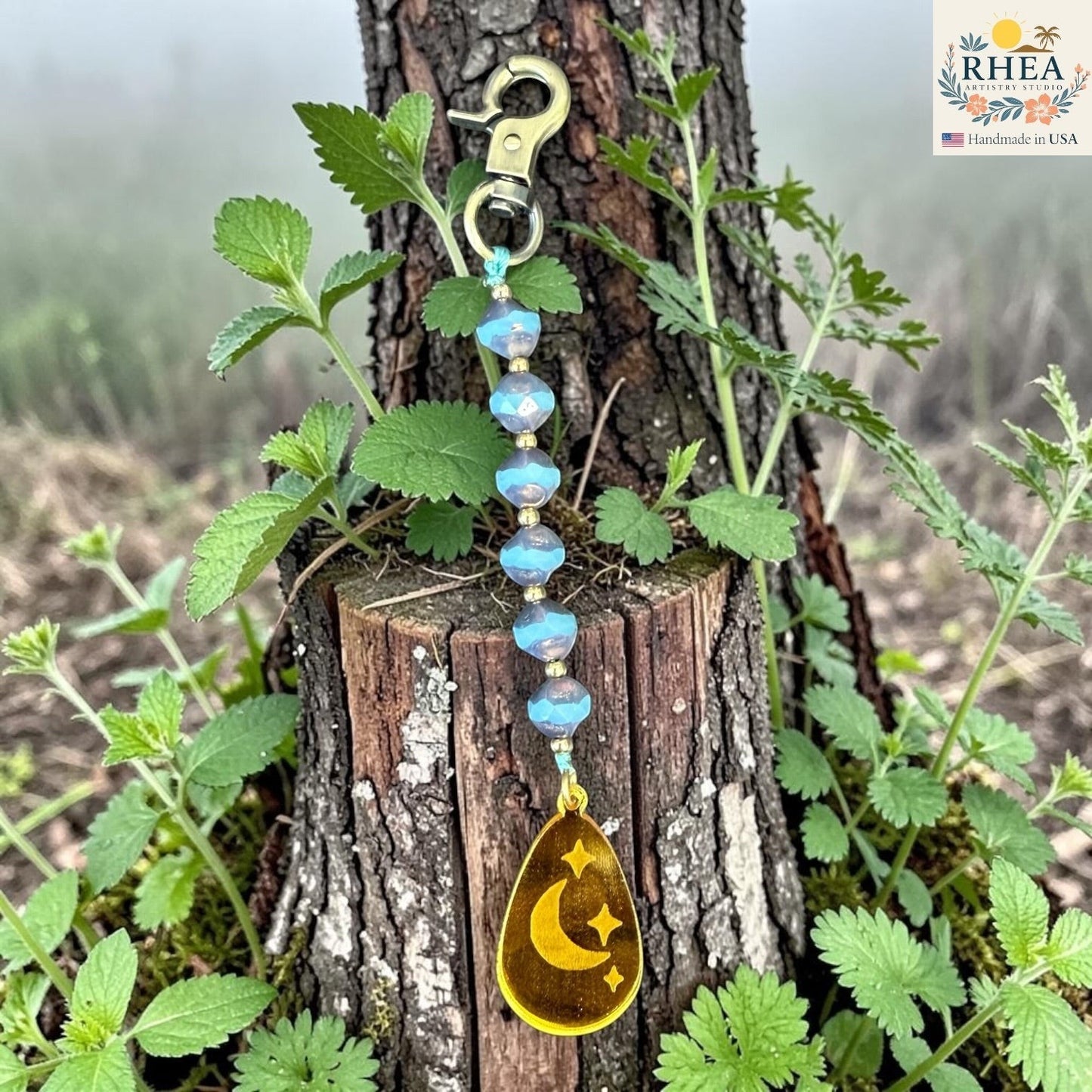 Rhea Artistry Studio blue Czech glass bead bag charm with brass accents and a gold pendant featuring a crescent moon and stars.