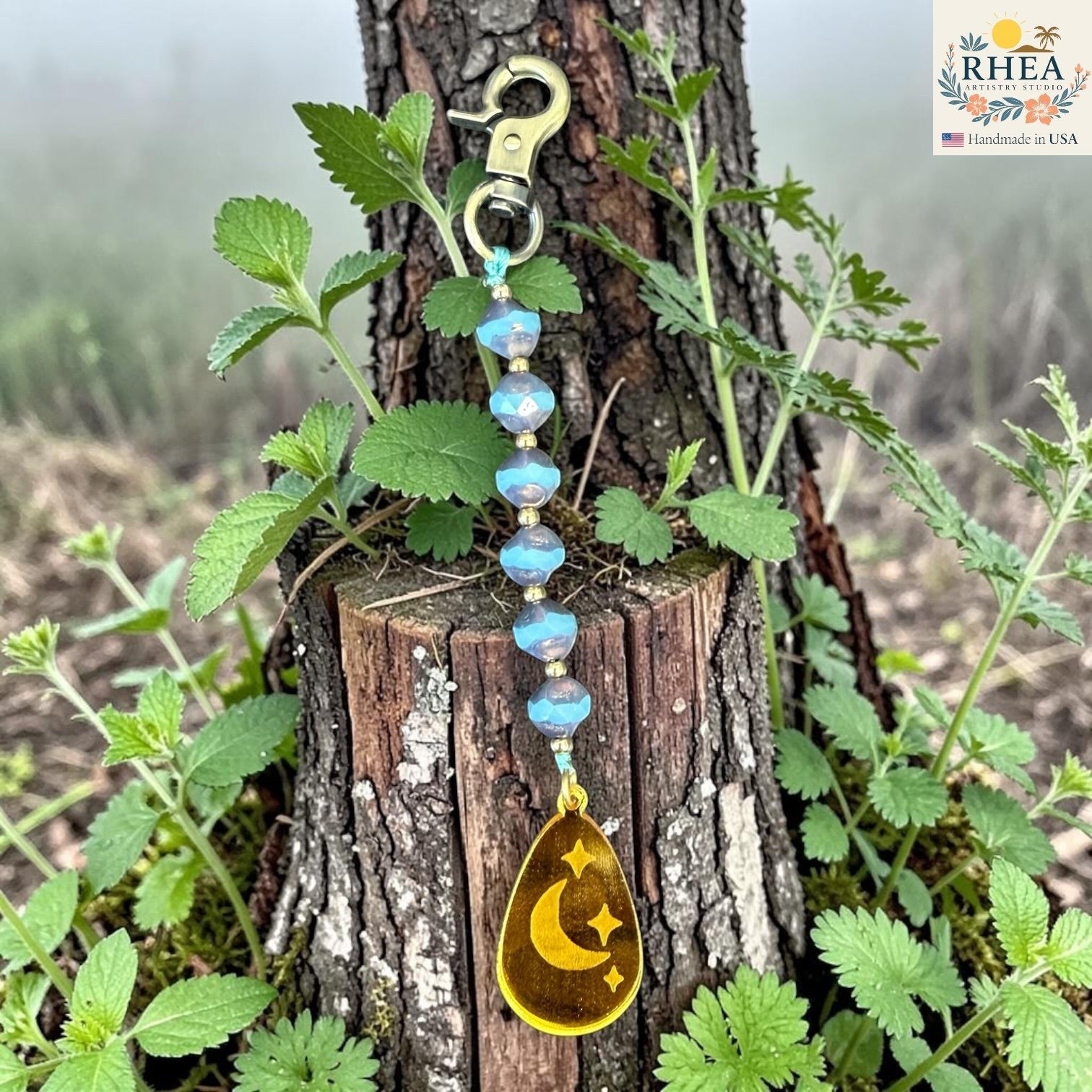 Rhea Artistry Studio blue Czech glass bead bag charm with brass accents and a gold pendant featuring a crescent moon and stars.