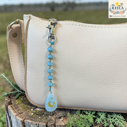 Rhea Artistry Studio blue Czech glass bead bag charm with hand-painted moon and stars pendant.