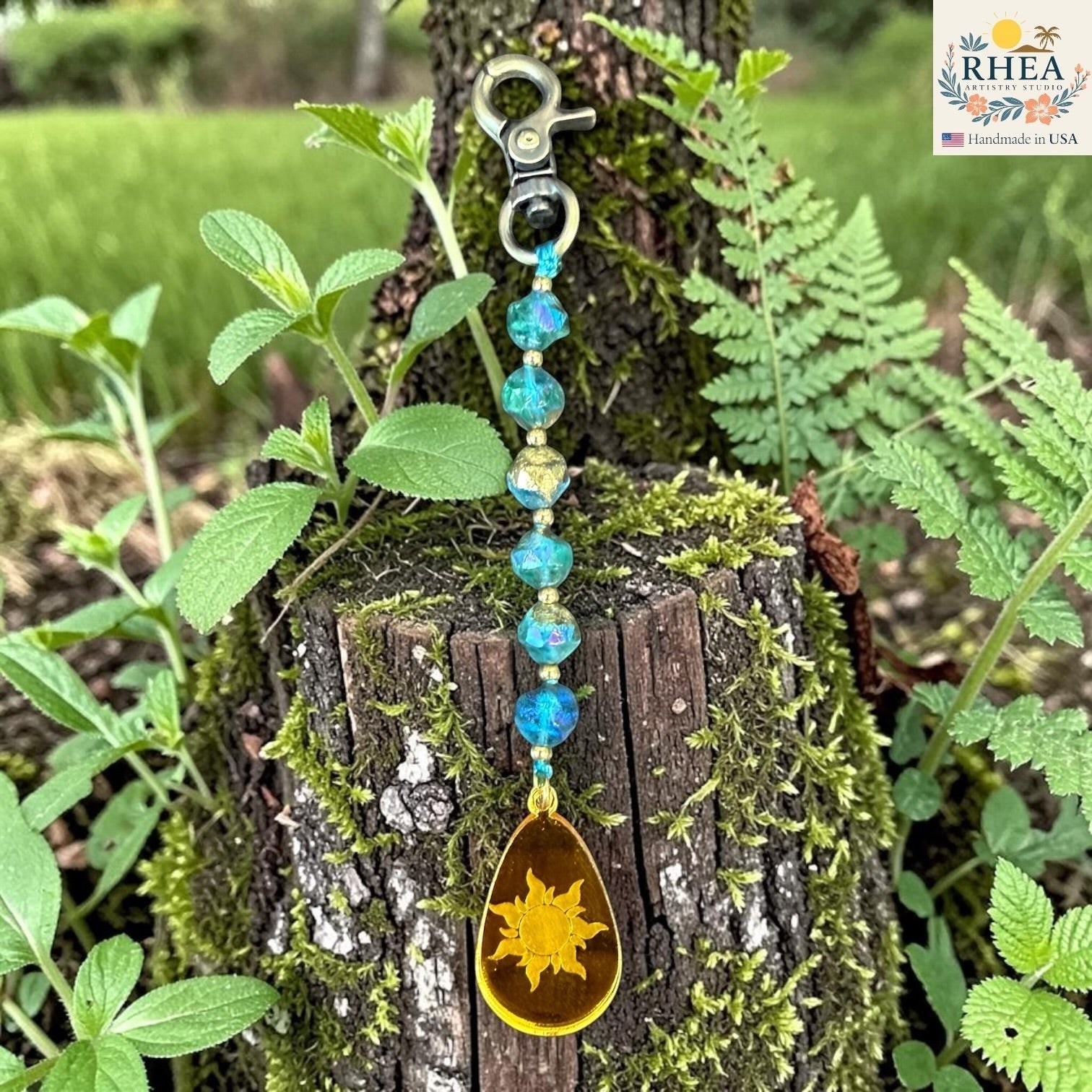 Rhea Artistry Studio blue Czech glass bead bag charm with brass accents and a hand-painted sun pendant.